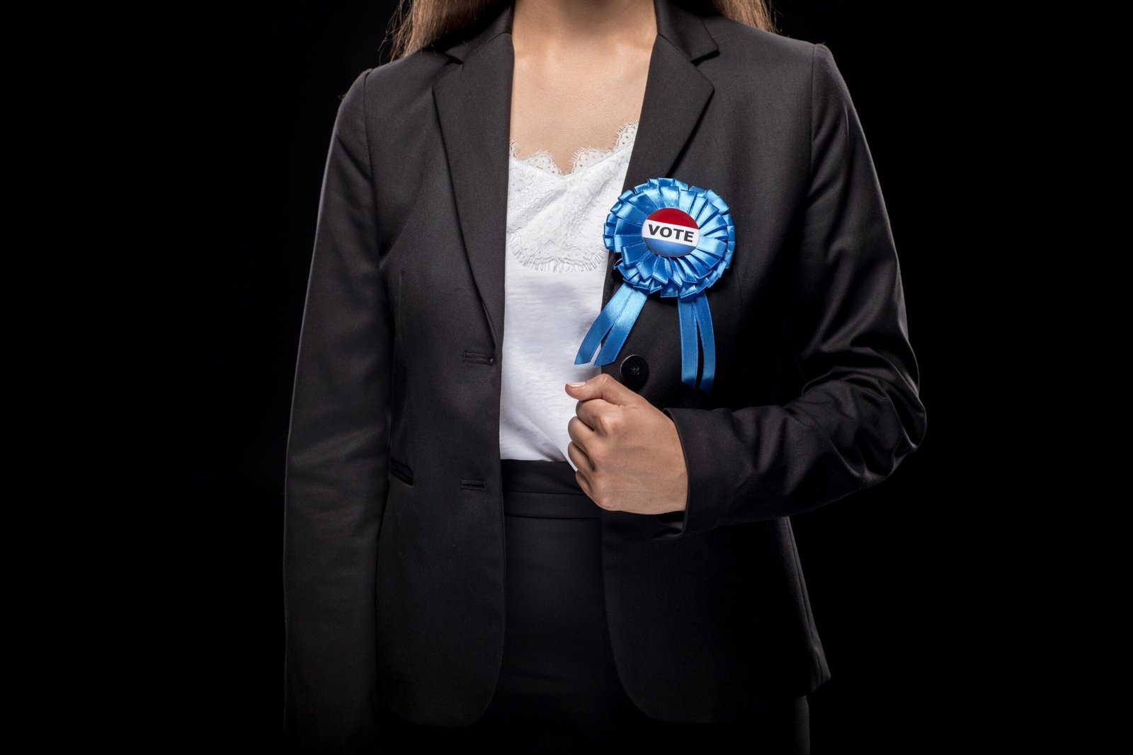 cropped view of businesswoman in black suit with vote badge, isolated on black